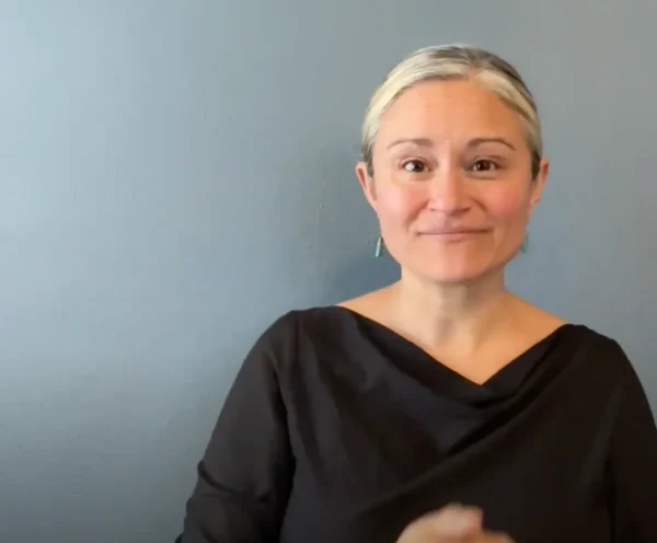 A screenshot of a white woman with blonde hair, from the Bridges Oregon organization, using ASL to sign a press release.